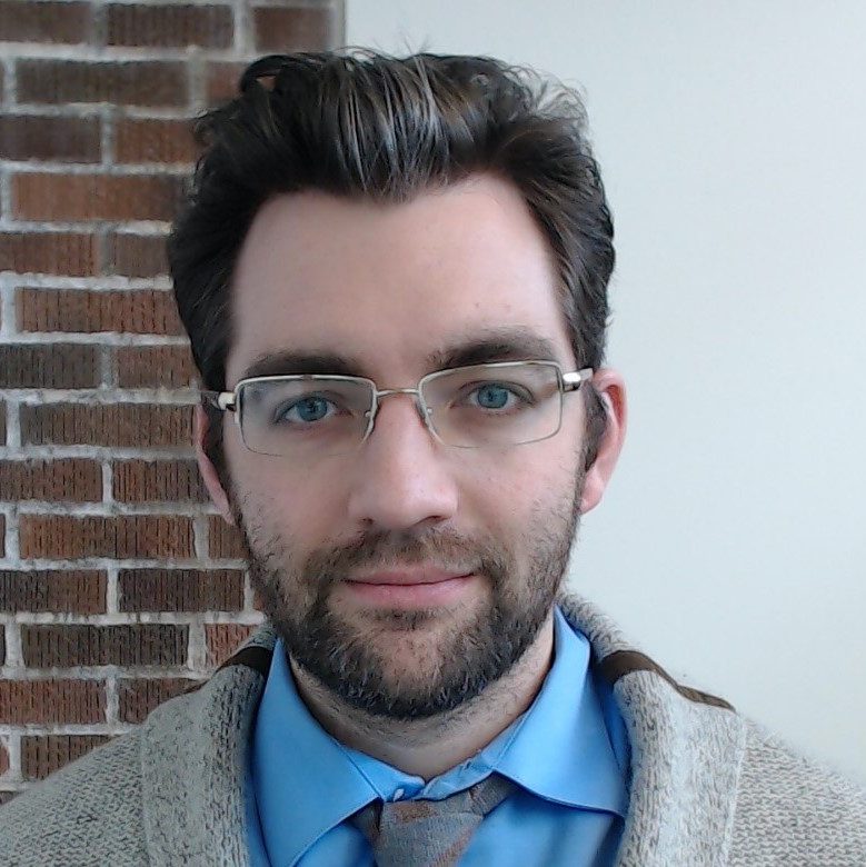 Headshot of Jeremy Winn. Jeremy has dark hair and a beard with a mustache.  He is wearing glasses and a shirt and tie.