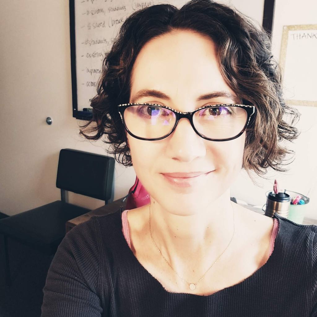 Headshot of Stephanie Bartlett smiling.  Stephanie has dark medium length wavy hair and is wearing glasses.